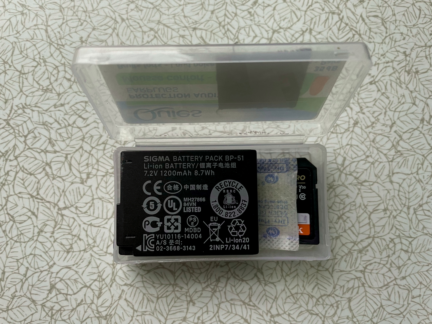 Plastic box with spare battery and SD card.